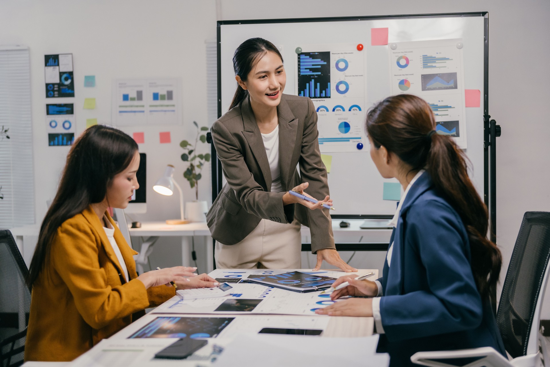 Three asian businesswomen are discussing charts and analyzing statistics during a meeting in a modern office, collaborating on important business decisions